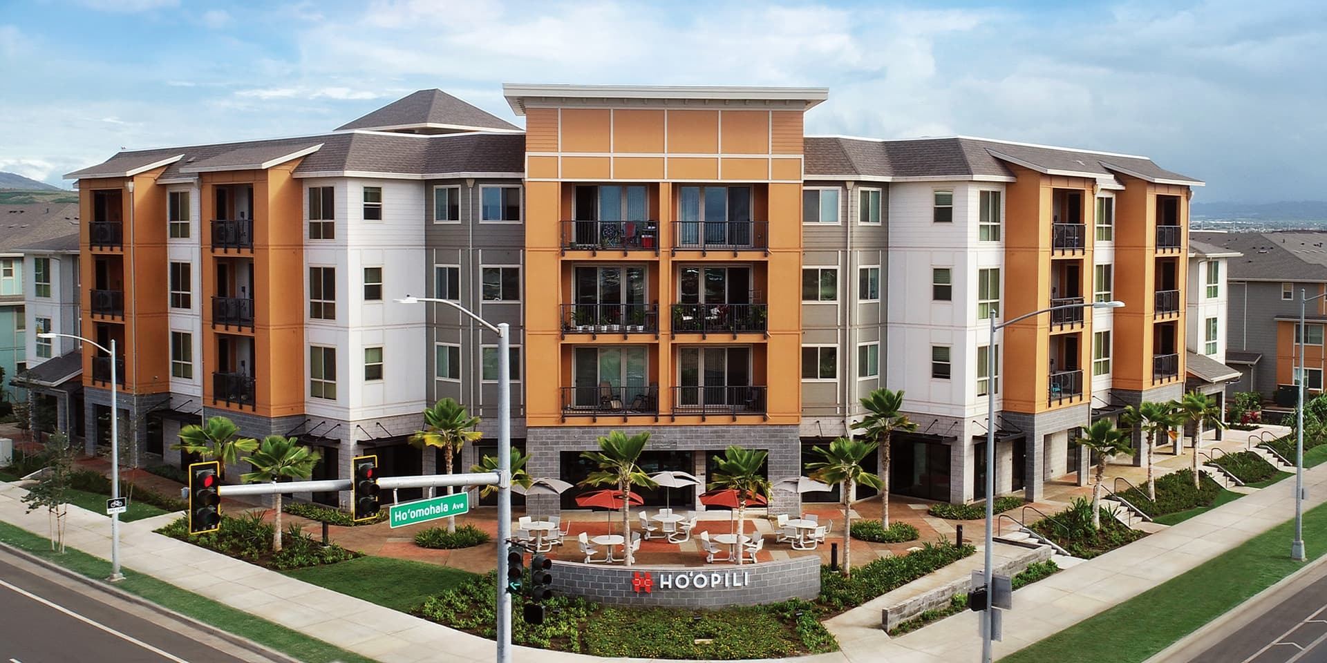 Hoʻopili residences with orange and gray façades, balconies and a landscaped gathering plaza along Hoʻomohala Avenue
