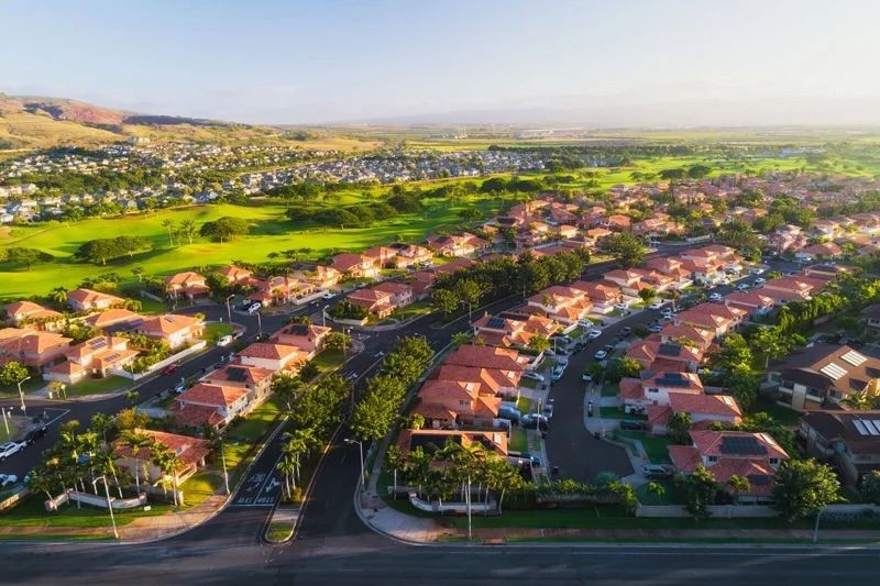 Aerial view of Kapolei homes and palm-lined streets beside green golf course fairways